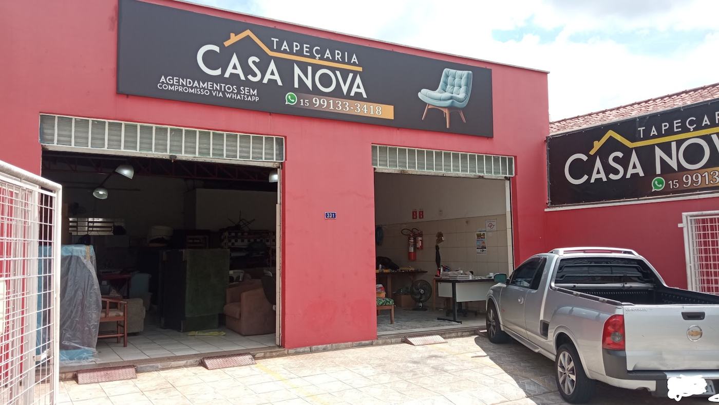 Fachada vermelha com o letreiro Tapeçaria Casa Nova e portas abertas para a oficina