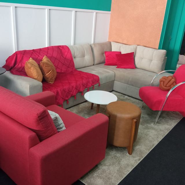 Sofá de canto bege com poltronas vermelhas e puff